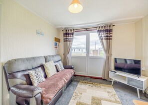 Een woonkamer met een bank, televisie en uitzicht door een raam.