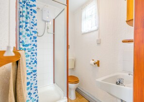 Een badkamer met douche, toilet, wastafel en een raam.