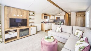 Een moderne woonkamer met een flatscreen televisie, houten kasten, een bank en een keukenhoek.