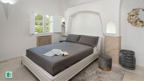 A bedroom with a bed, a window, a radiator, a small stool, and a decorative wall piece. - COZY VILLA FLORA - PRIVATE POOL AND WALKING DISTANCE FROM THE BEACH (San Teodoro)
