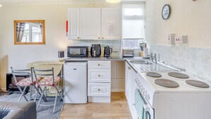 A compact kitchen with white cabinets, a microwave, a toaster, a sink, and a stove. - 1 bedroom accommodation in Anderby Creek, Mablethorpe (Anderby Creek, Mablethorpe)