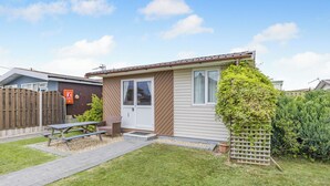 A small, single-story house with a front door, a small porch, a picnic table, and a fenced yard. - 1 bedroom accommodation in Anderby Creek, Mablethorpe (Anderby Creek, Mablethorpe)