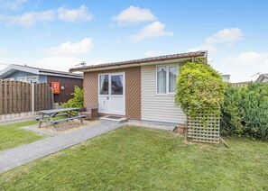 Ein kleines, eingeschossiges Haus mit Haustür, einer kleinen Veranda, einem Picknicktisch und einem umzäunten Garten.