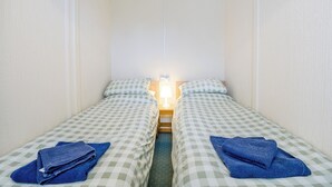 A small, narrow room with two single beds, each with a checkered bedspread and a blue towel. - 1 bedroom accommodation in Anderby Creek, Mablethorpe (Anderby Creek, Mablethorpe)