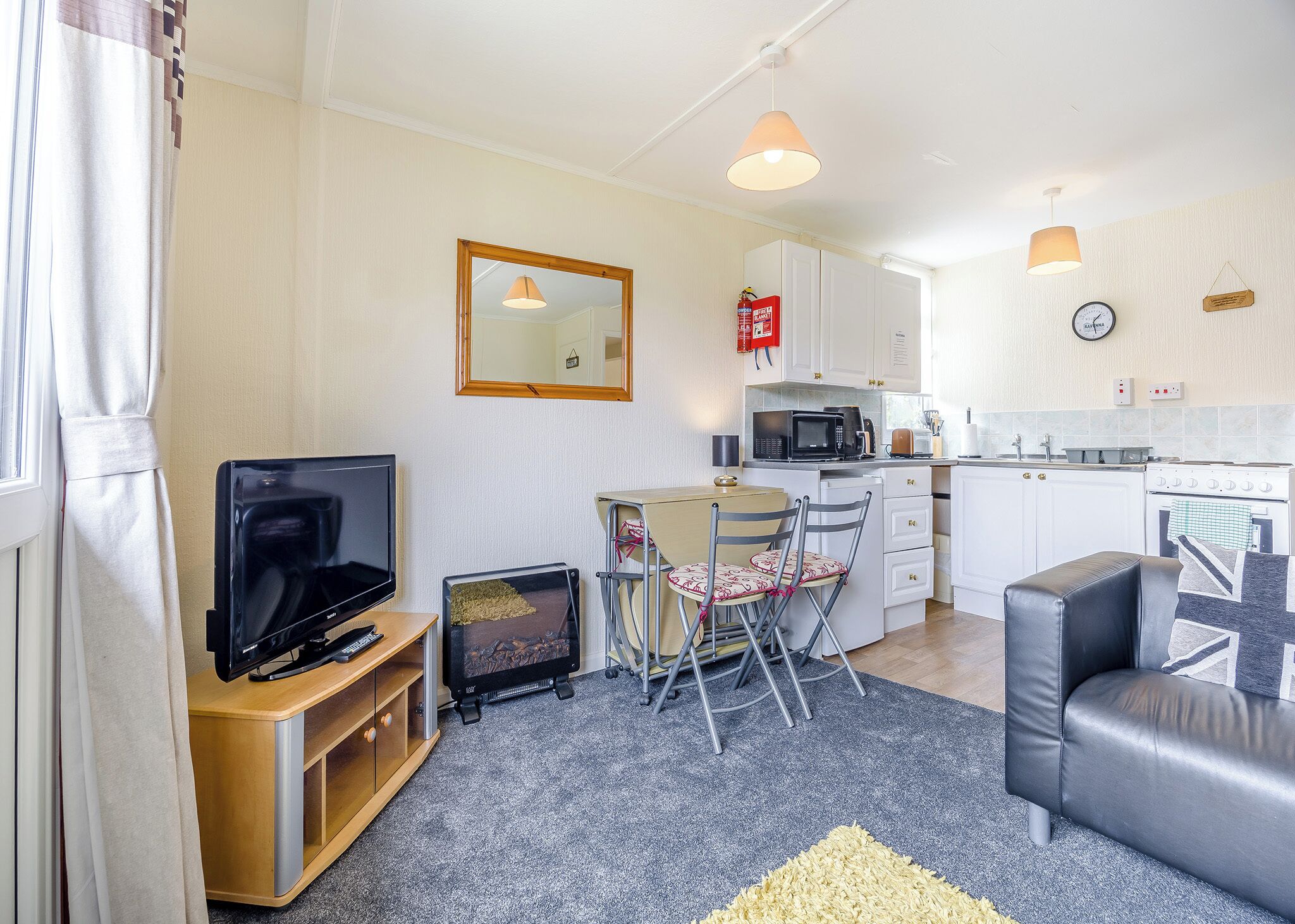 A compact living space with a television, a small dining table, a sofa, and a kitchenette.