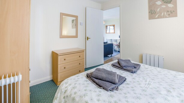 Une chambre à coucher avec un lit, une commode en bois, un miroir et un radiateur.