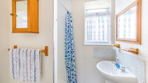 A bathroom with a wooden cabinet, a towel rack with a patterned towel, a shower curtain, a window with lace curtains, and a sink with a bottle of hand soap. - 1 bedroom accommodation in Anderby Creek, Mablethorpe (Anderby Creek, Mablethorpe)