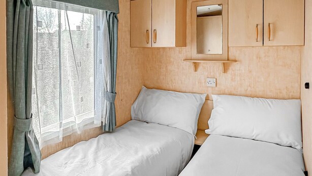 Une chambre avec deux lits, une fenêtre avec des rideaux et des armoires en bois.