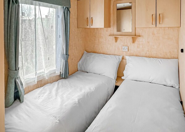 A bedroom with two beds, a window with curtains, and wooden cabinets.