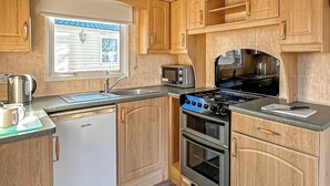 Une cuisine compacte équipée d’un lave-vaisselle, d’une cuisinière, d’un four, d’un four à micro-ondes et d’une fenêtre avec des stores.