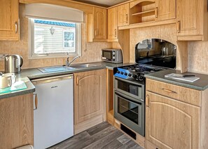 A compact kitchen with a dishwasher, stove, oven, microwave, and a window with blinds.