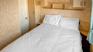 Una cama individual con ropa de cama blanca, cabecera de madera y mesita de noche de madera con una lámpara.