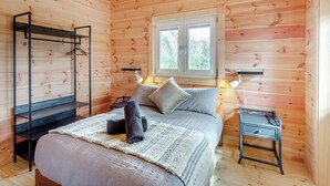 Une chambre dans une cabane en bois, avec un lit, des tables de chevet, un porte-vêtements et une fenêtre.