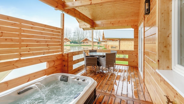 Une terrasse en bois avec un jacuzzi, des sièges d’extérieur et une vue sur les chalets.