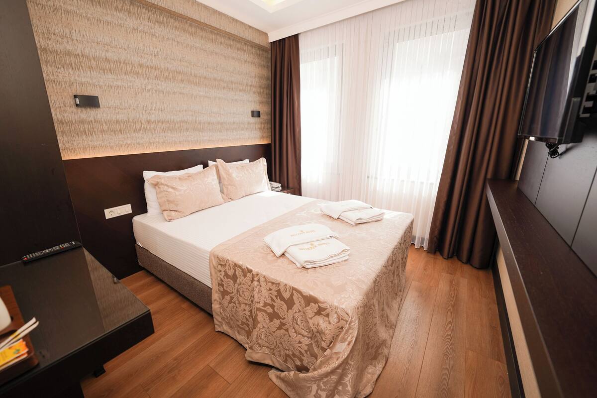 A hotel room with a large bed, a flat-screen TV, a wooden desk, and a water bottle on the nightstand.