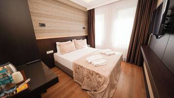 A hotel room with a large bed, a flat-screen TV, a wooden desk, and a water bottle on the nightstand.
