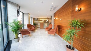 Um saguão de hotel com balcão de recepção, área de estar e plantas em vasos.