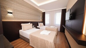 Quarto de hotel com duas camas, uma televisão e piso de madeira.