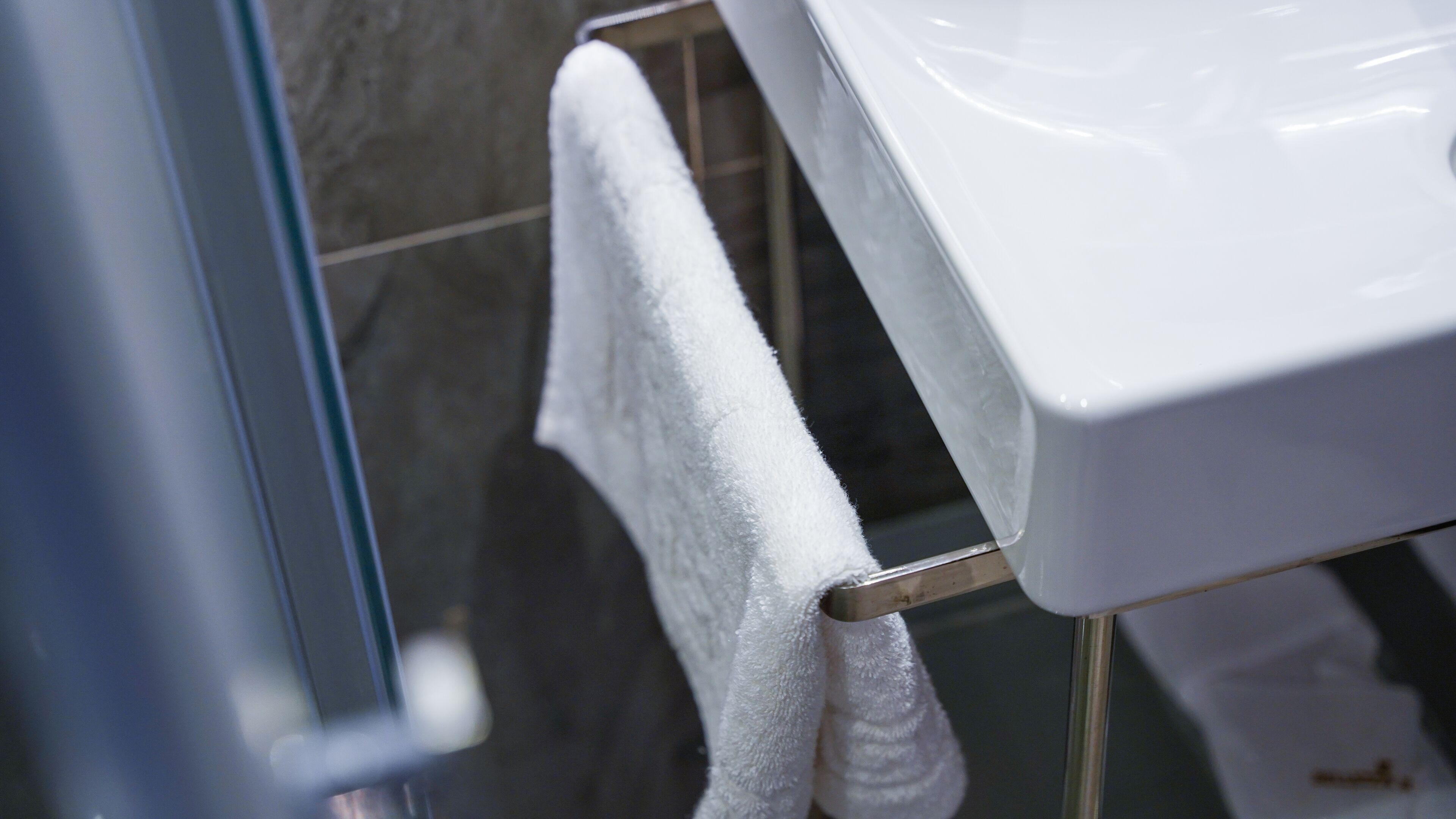 A white bathroom sink with a towel hanging on a metal towel rack.