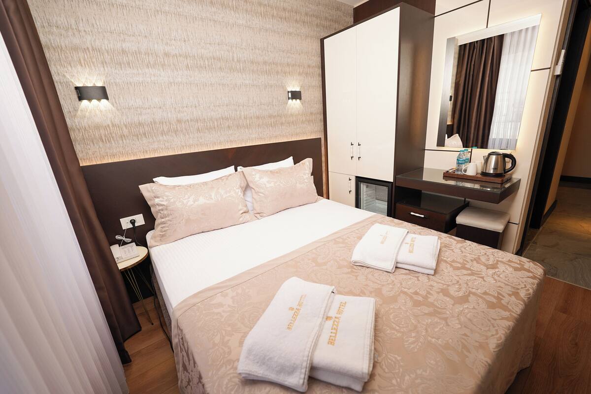 A hotel room with a bed, a desk, a mirror, and a nightstand with a phone.