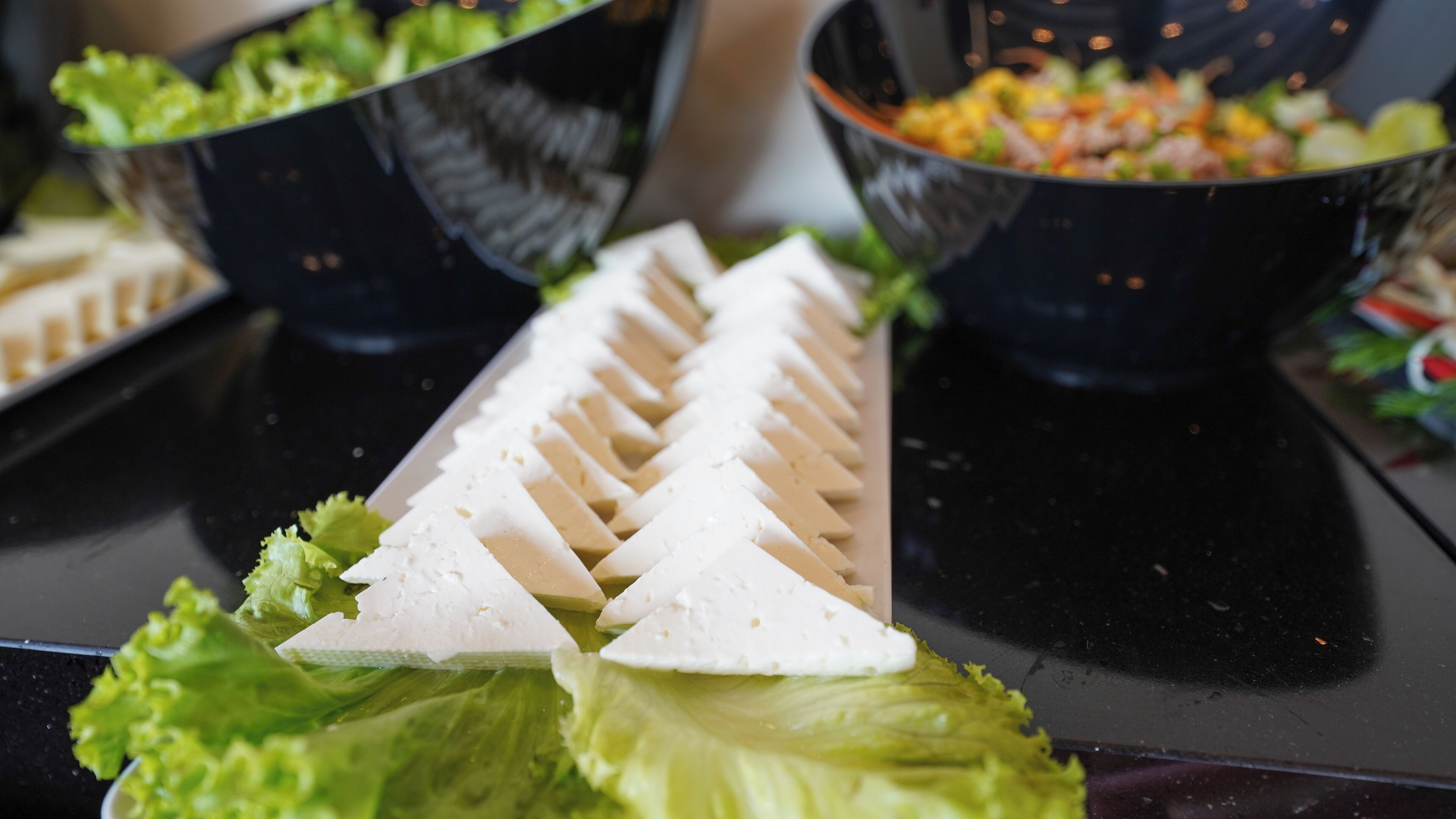 A buffet table with various dishes, including a salad and sliced white food, possibly tofu, arranged on a black table.