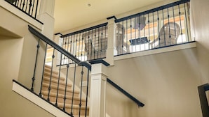 A staircase with a beige carpet and black balusters, leading to a landing with a white wall and a light switch. - Hilltop Home on Lake Whatcom | Views, Beach Access & Space for Ten (Bellingham)