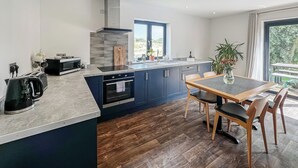 A modern kitchen with a central island, built-in oven, and a dining area with a table and chairs. - 1 bedroom accommodation in Old Buckenham (Old Buckenham)
