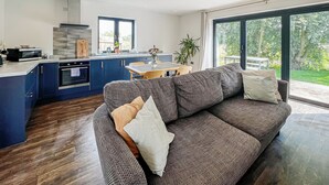 A modern kitchen with blue cabinets, a built-in oven, and a dining area with a table and chairs. - 1 bedroom accommodation in Old Buckenham (Old Buckenham)
