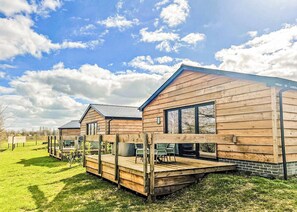 A row of wooden cabins with a deck, large windows, and a grassy area in the background.