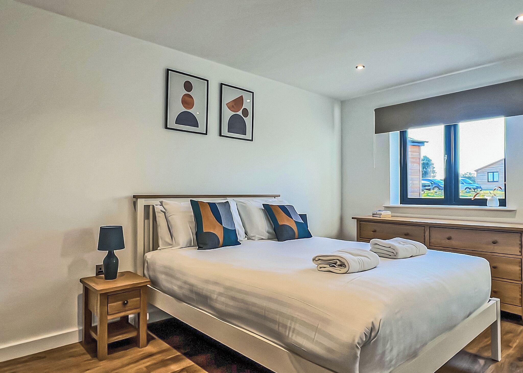 Une chambre à coucher avec un lit, des tables de chevet, une fenêtre et des œuvres d’art accrochées au mur.