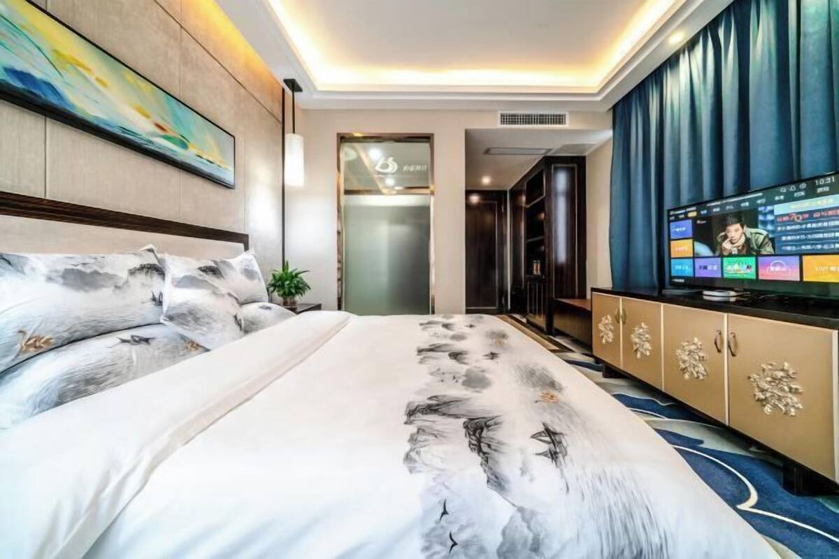 A hotel room with a large bed, a TV, a wardrobe, and a painting on the wall.