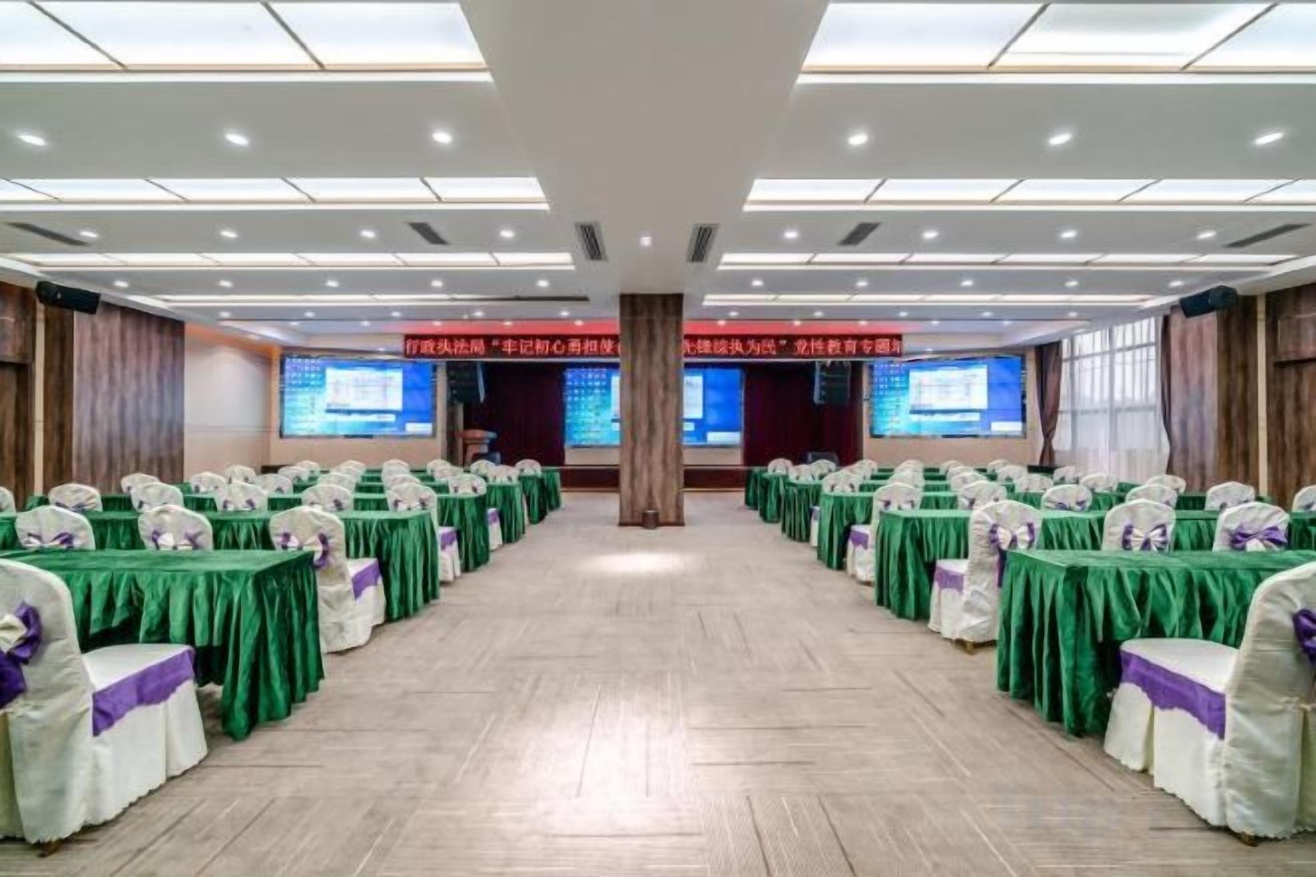 A conference room with rows of tables and chairs, large screens at the front, and a stage.