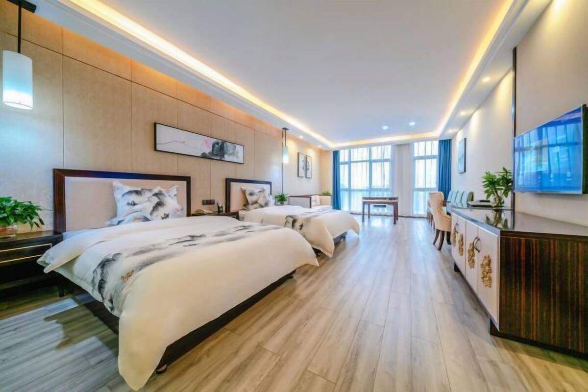 A modern hotel room with two beds, a desk, and a TV.
