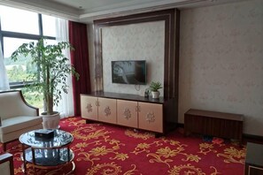 A hotel room with a large window, a flat-screen TV mounted on the wall, a potted plant, a sofa, a round coffee table, and a carpeted floor. - Bohao Hotel (Zunyi)
