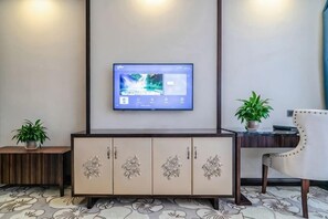 A modern interior with a flat-screen TV mounted on the wall, a wooden cabinet with decorative handles, a potted plant, and a chair with a cushion. - Bohao Hotel (Zunyi)