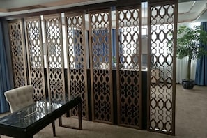 A room with a glass table, a chair, a potted plant, and a decorative screen.