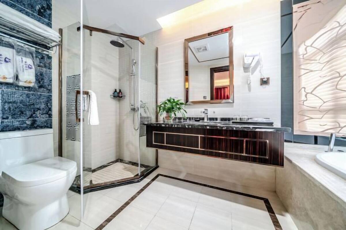 A modern bathroom with a glass shower enclosure, a white toilet, a vanity with a dark wood finish, and a large mirror.