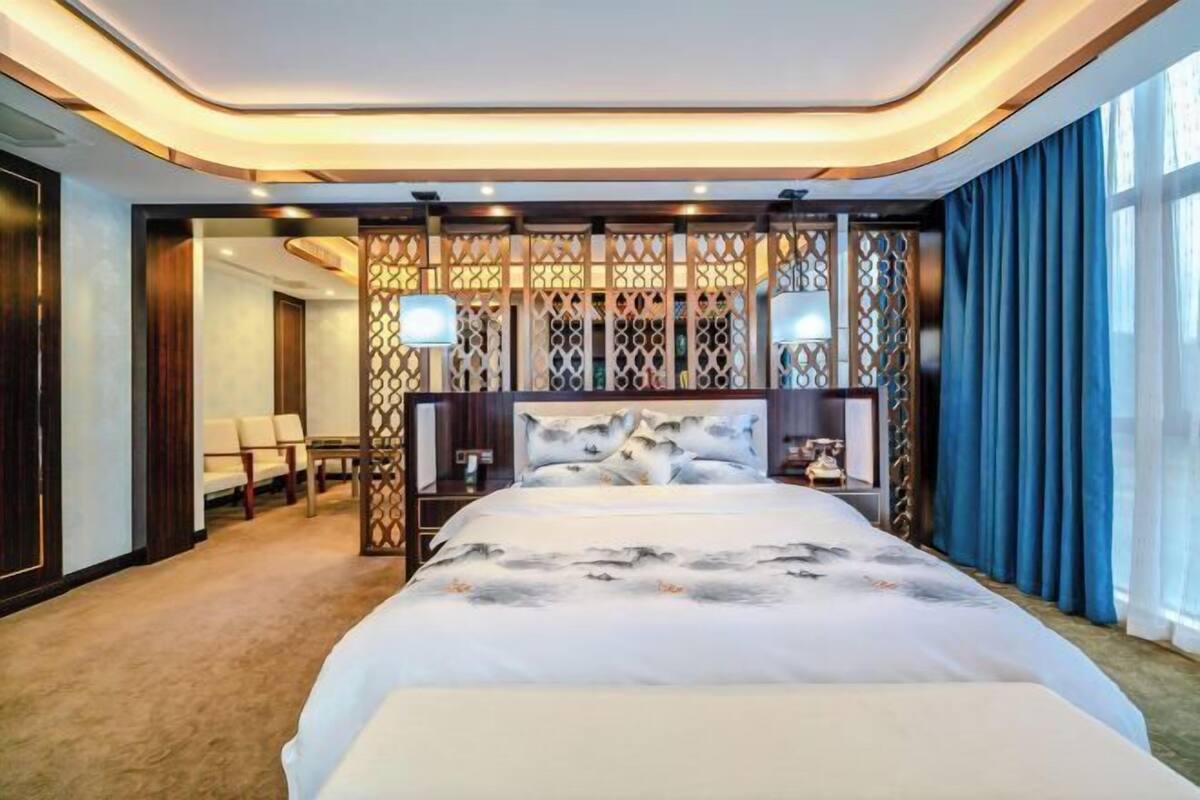 A hotel room with a large bed, a decorative partition, and a view of the outside.