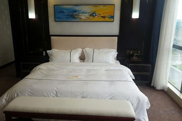 A hotel room with a large bed, a bedside table, a nightstand, and a painting on the wall.