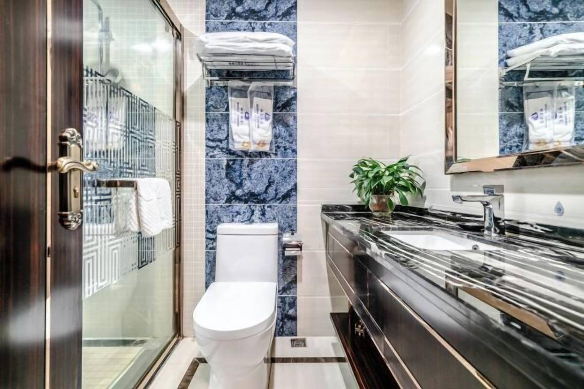 A modern bathroom with a glass shower enclosure, a white toilet, a black vanity with a mirror, and a potted plant.