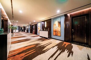 A hotel corridor with a patterned carpet, wooden doors, and artwork on the walls. - Bohao Hotel (Zunyi)