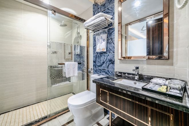 A modern bathroom with a glass shower enclosure, a white toilet, a marble-tiled wall, and a black countertop with a sink and mirror.