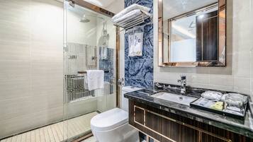 A modern bathroom with a glass shower enclosure, a white toilet, a marble-tiled wall, and a black countertop with a sink and mirror.