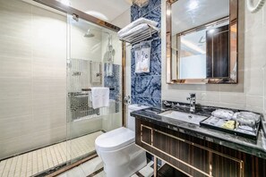 Un baño moderno con cabina de ducha de vidrio, inodoro blanco, pared con azulejos de mármol y encimera negra con lavamanos y espejo.