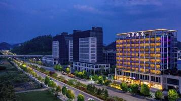 A modern hotel with multiple floors, a well-lit facade, and a surrounding landscaped area.