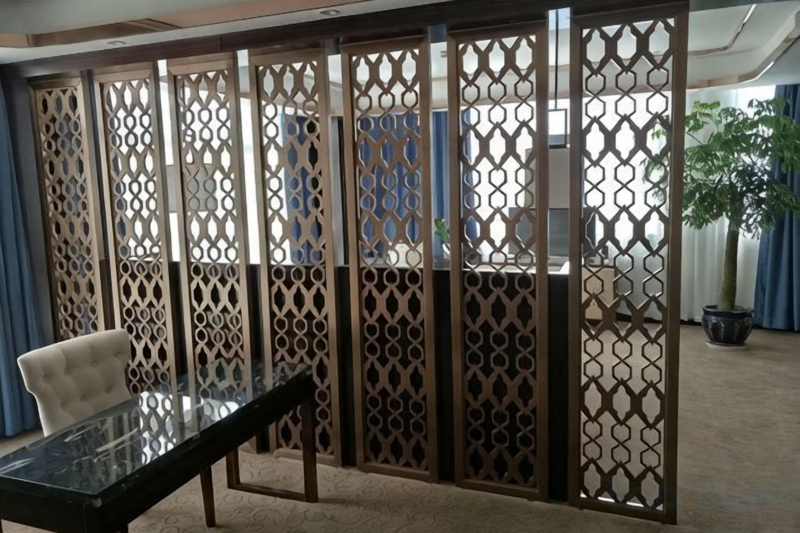 Een kamer met een glazen tafel, een stoel en een decoratieve scheidingswand met een geometrisch patroon.