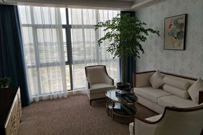 Una habitación de hotel con un ventanal grande, un sofá, una silla, una mesa de centro y una planta en maceta.