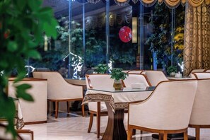 A restaurant with a glass table and chairs, surrounded by plants and decorative lights. - Bohao Hotel (Zunyi)