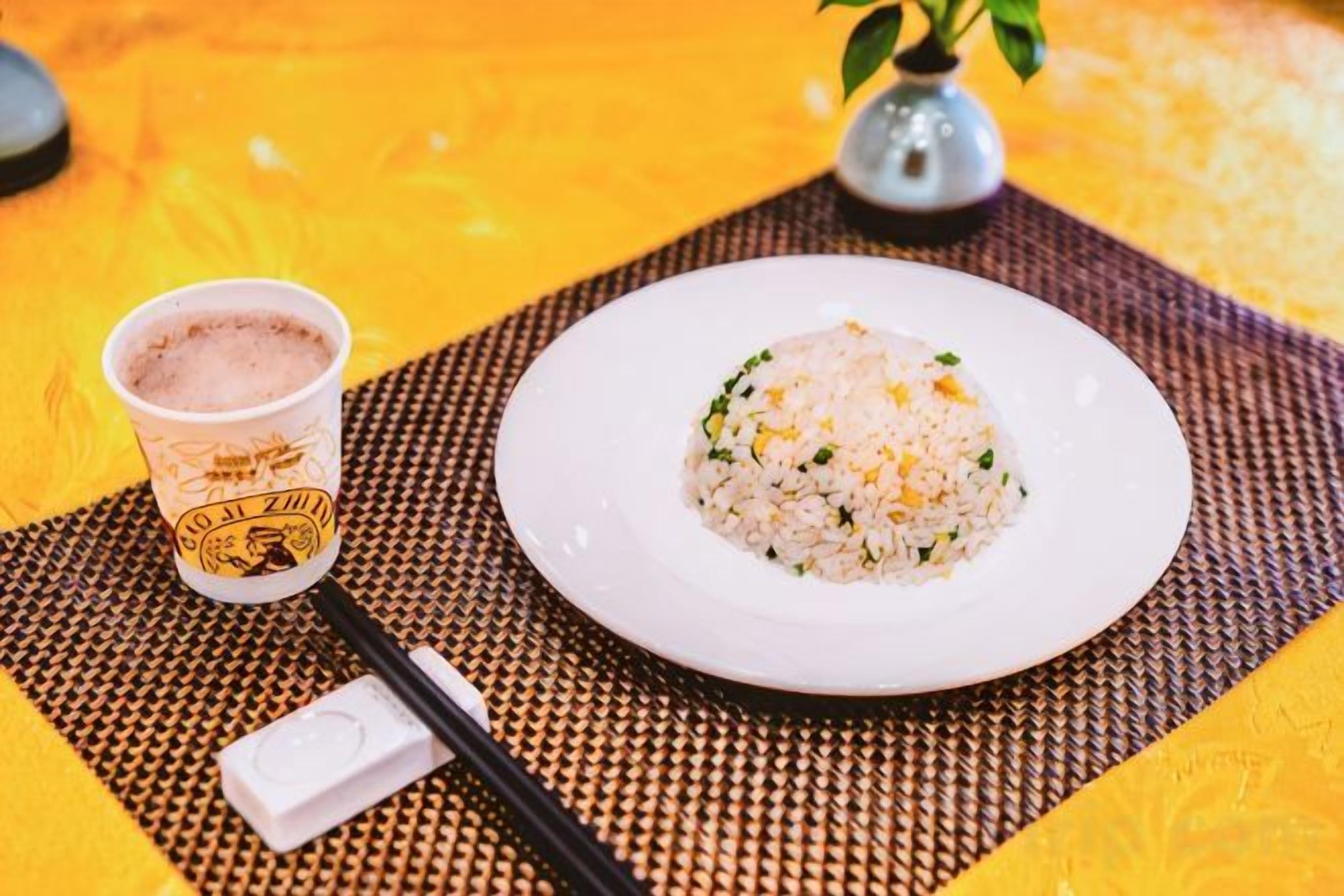 Une assiette de riz, une tasse de café et des baguettes sur une table jaune.