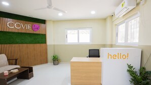 A reception area with a wooden reception desk, a 'hello!' sign, a plant, and a 'COVIE' sign on the wall. - Covie Karle Town 220 (Bengaluru)